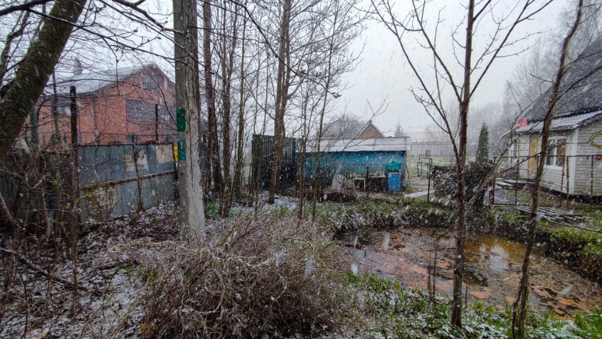 Хозяйственные постройки и деревья у пруда во время снегопада