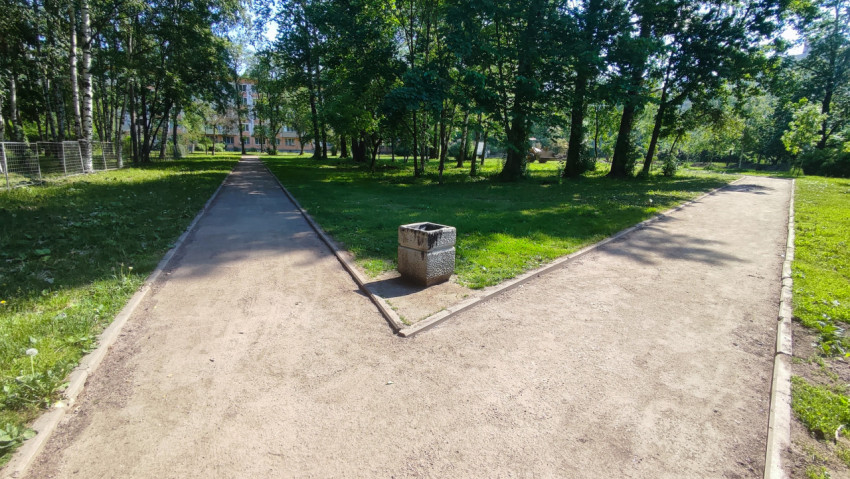 Парк с развилкой пешеходных дорожек и урной в центре развилки