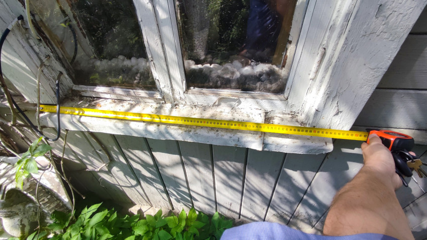 Измерение ширины окна деревянного дома рулеткой