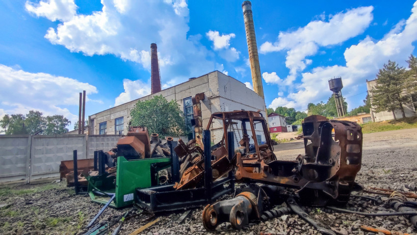 Ржавые фрагменты техники на фоне промышленного здания с дымовыми трубами
