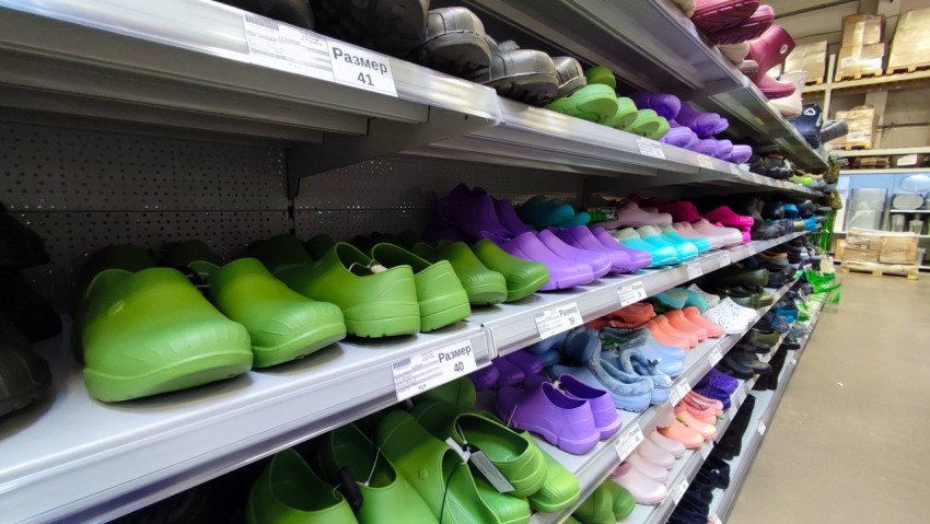 Ряды разноцветных садовых сабо и галош в хозяйственном магазине