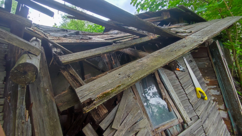 Перекошенная стена с окном и ручной пилой на заброшенной постройке