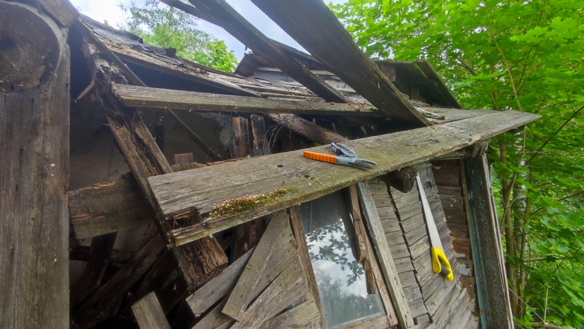 Окно и обломки обшивки под разрушенной крышей старой деревянной постройки