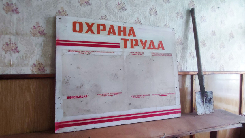 Стенд «Охрана труда» и лопата у стены в старом помещении