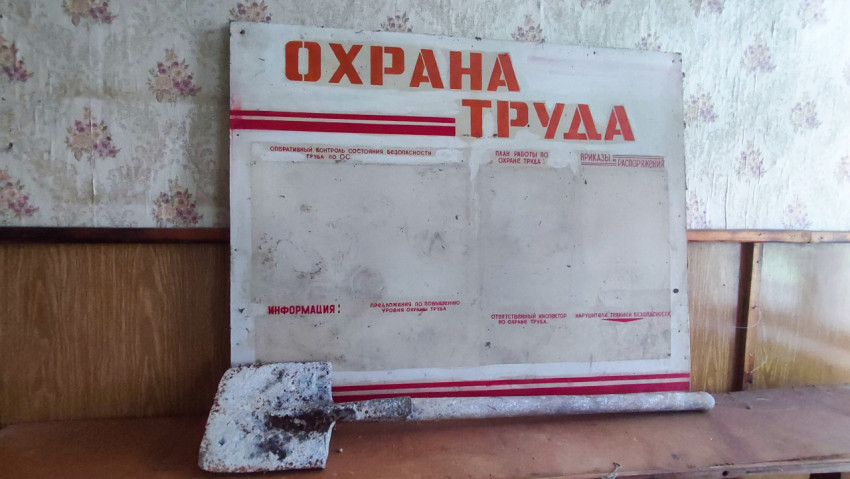 Стенд «Охрана труда» под углом и лопата на столешнице в пустой комнате