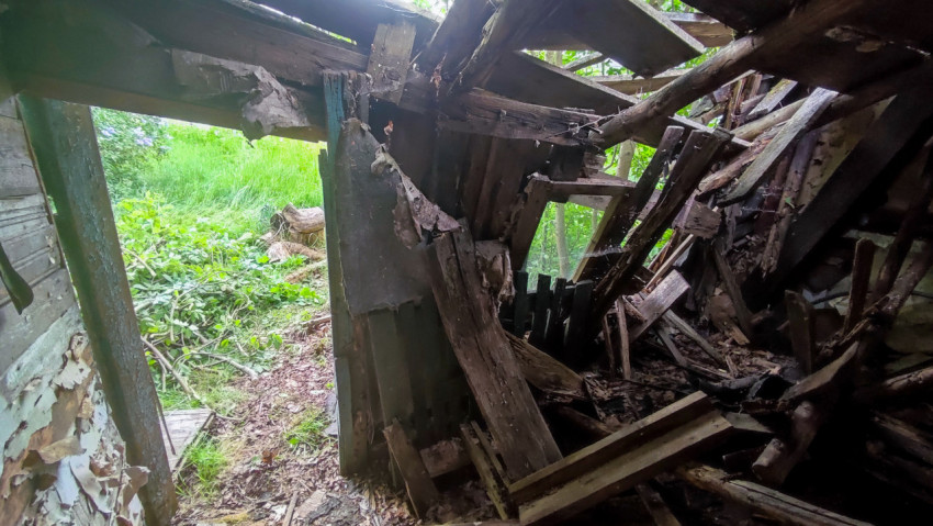 Интерьер заброшенной постройки с завалом досок и дверным проёмом в сад