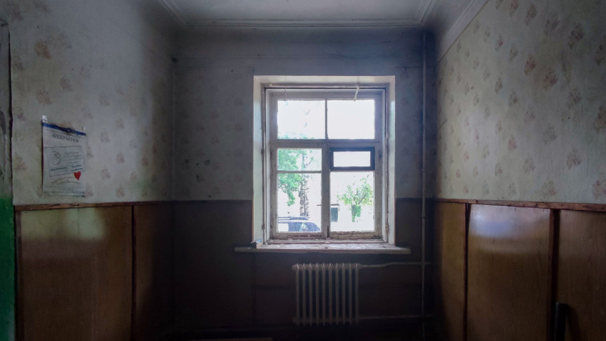 Окно с видом на деревья в пустующей комнате с радиатором, панелями и плакатом на стене