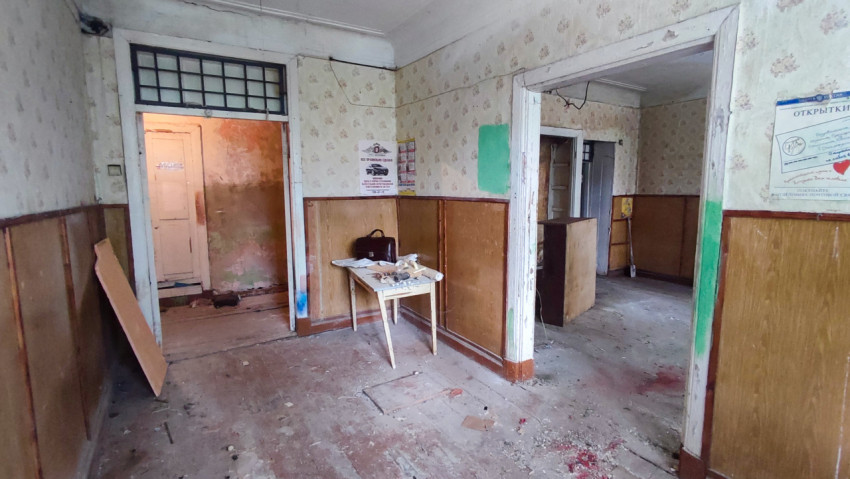 Заброшенная комната с деревянными панелями, дверными проёмами и столом посередине