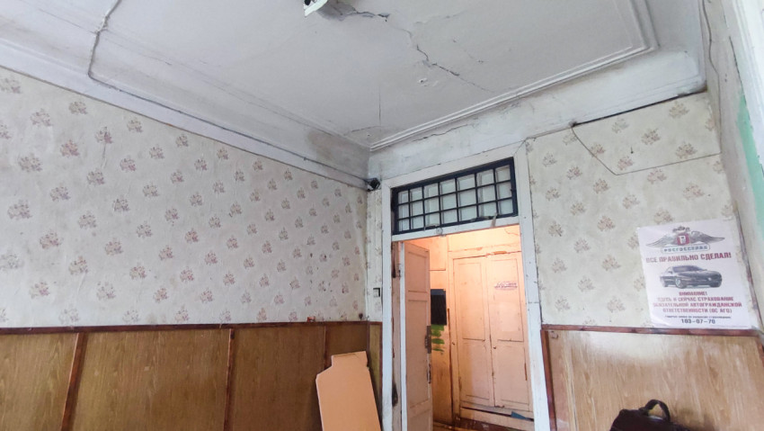 Старый интерьер с трещинами на потолке, дверью с фрамугой и плакатом про ОСАГО