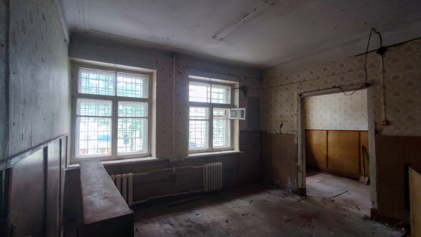 Комната с двумя окнами в решётках, радиаторами и следами демонтажа