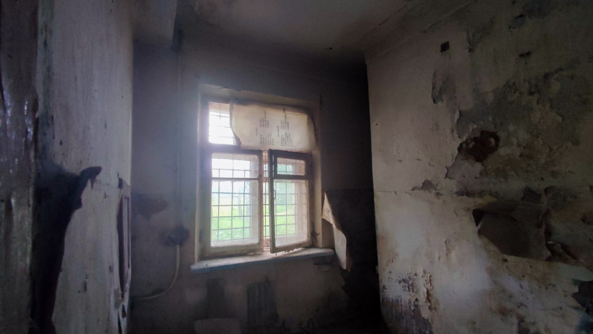 Тёмная комната с окном в решётке, приоткрытой створкой и следами сырости