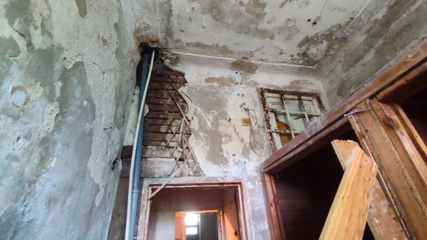 Угол помещения с открытой дранкой, трубой и ржавой оконной рамой над дверным проёмом