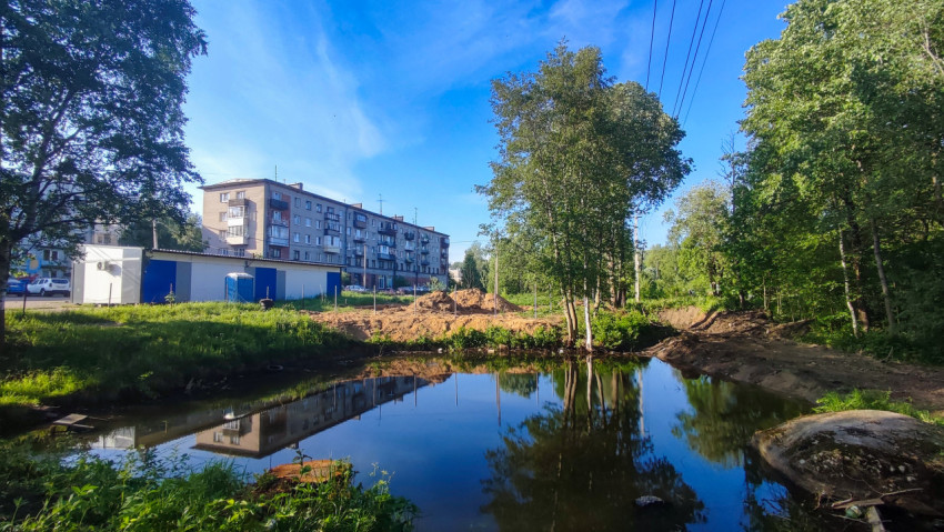 Пруд с отражением жилого дома и деревьев рядом со стройплощадкой