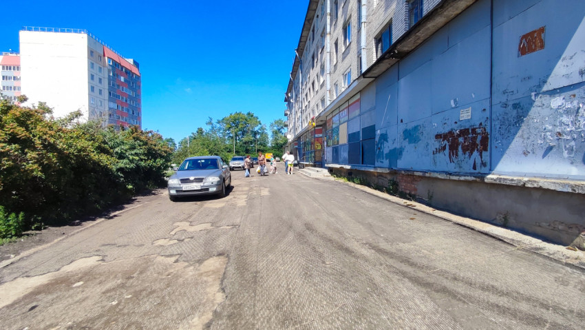 Дворовая дорога вдоль жилого дома с витринами и пешеходами у магазина