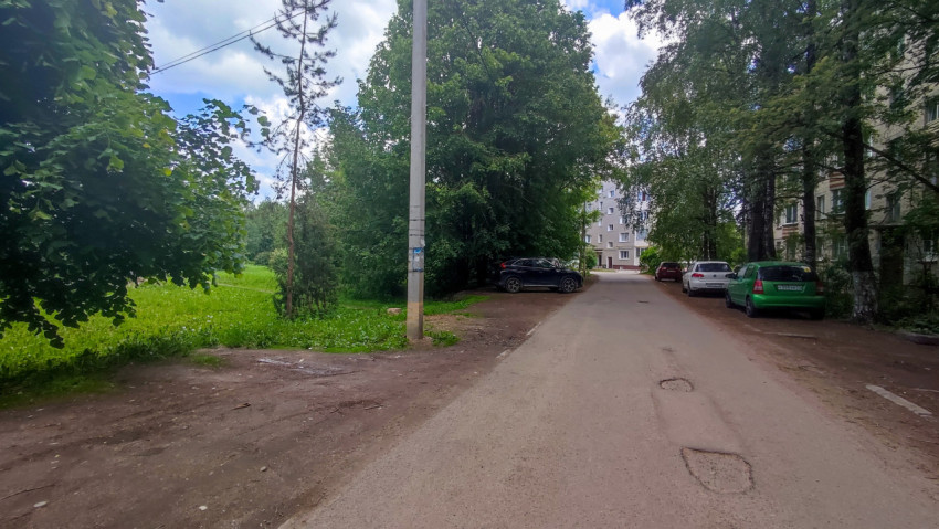 Асфальтовая дорога в жилом районе с бетонным столбом и припаркованными машинами