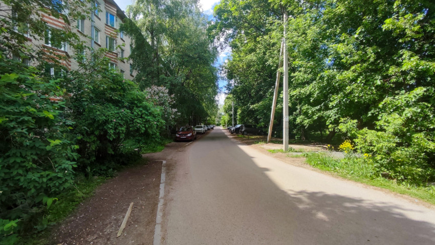 Дворовая дорога вдоль многоэтажного дома и зелёных насаждений с припаркованными автомобилями