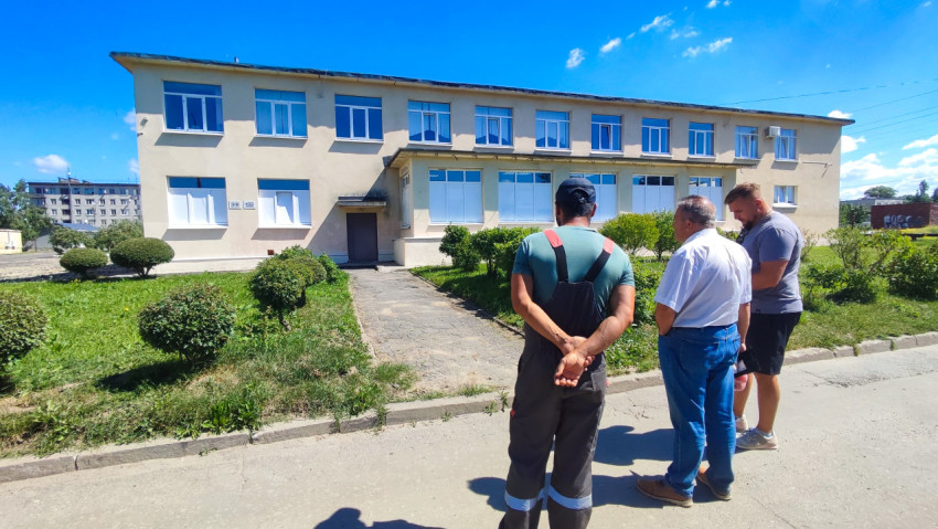 Три человека осматривают территорию перед двухэтажным административным зданием