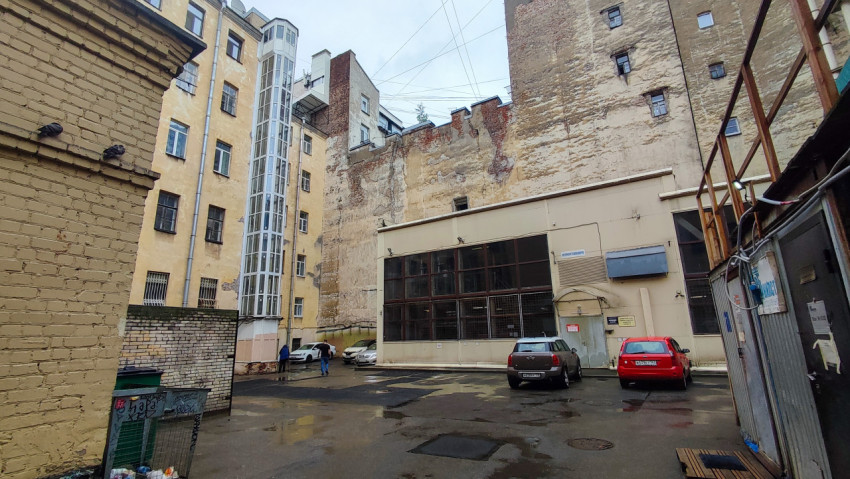 Двор между домами с внешней стеклянной шахтой лифта, лужами и припаркованными автомобилями