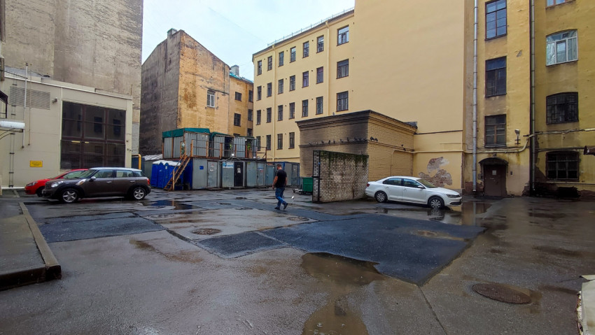 Общий вид двора со строительными бытовками, биотуалетами, лужами и припаркованными автомобилями