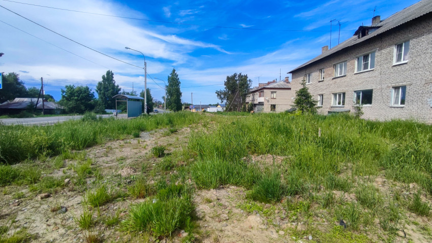 Улица с автобусной остановкой и кирпичным домом у заросшего пустыря