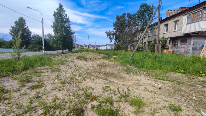 Разрытый участок грунта у дороги рядом с жилым домом и наклонной опорой
