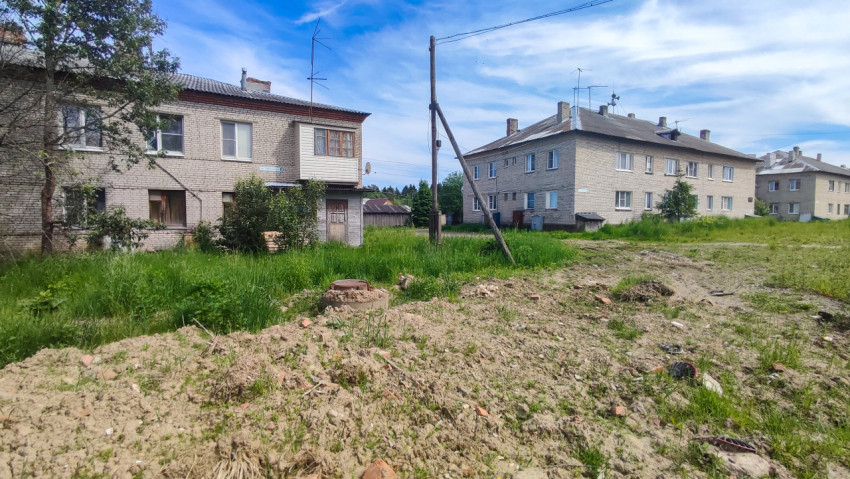Разрытый участок земли с колодцем и опорами связи между малоэтажными кирпичными домами