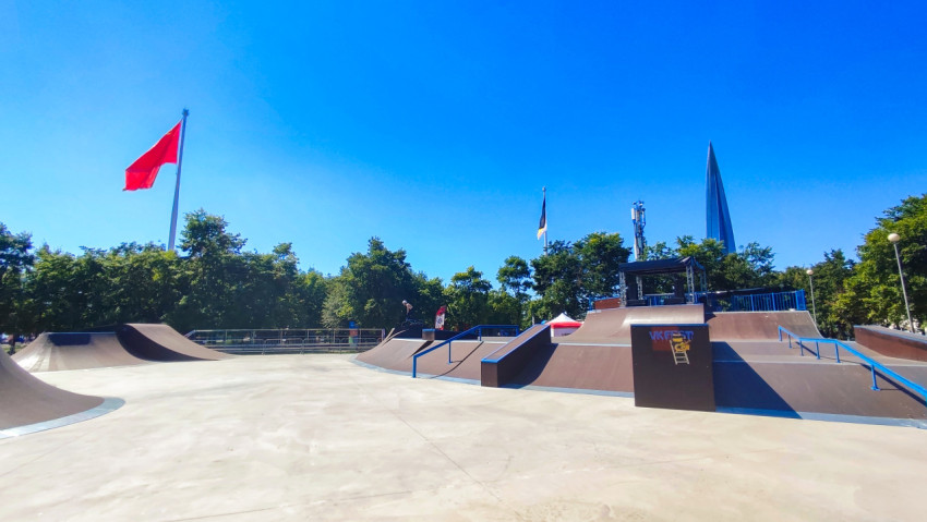 Площадка скейтпарка с фигурами и перилами в ясный день на фоне городской панорамы