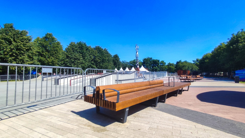 Длинная парковая скамейка у бетонного скейтпарка с ограждениями и шатрами