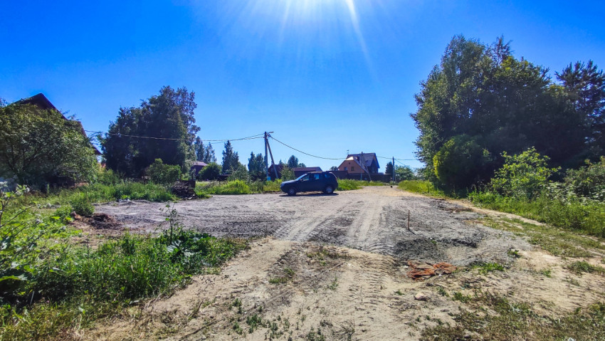 Грунтовая дорога с разровненной площадкой, автомобилем и линиями электропередачи в деревне