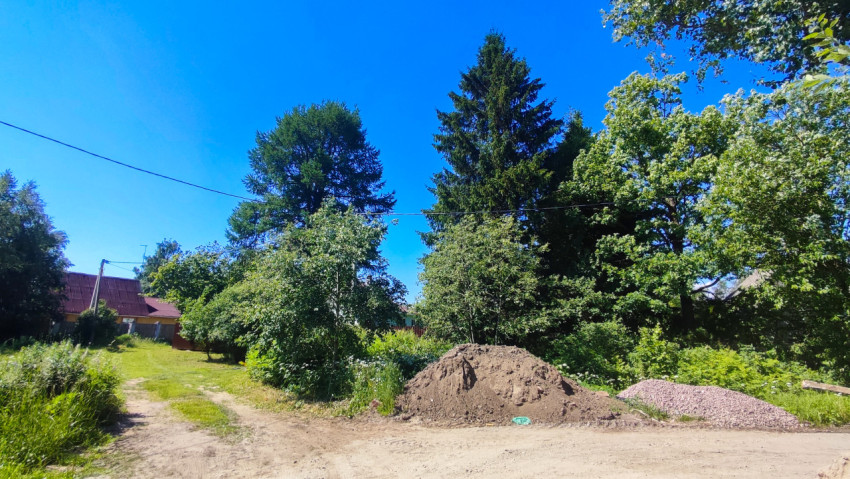 Куча грунта и насыпь щебня у грунтовой дороги рядом с частным домом и деревьями