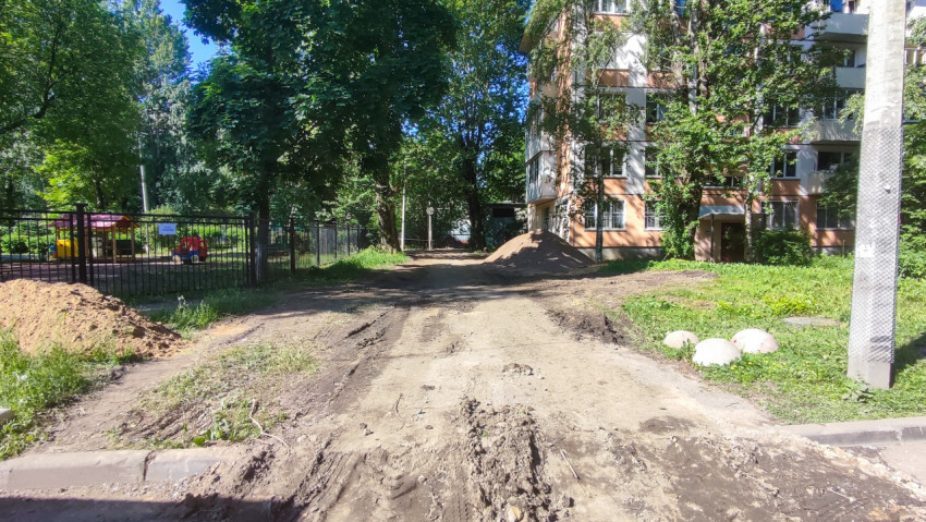 Разрытый дворовой проезд с кучами песка у жилого дома и детской площадки
