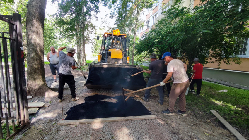 Рабочие распределяют горячий асфальт из ковша экскаватора-погрузчика во дворе дома