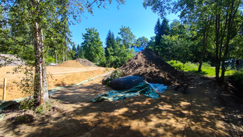 Строительная площадка в лесу с песчаной подсыпкой, кучами грунта и уложенным геотекстилем