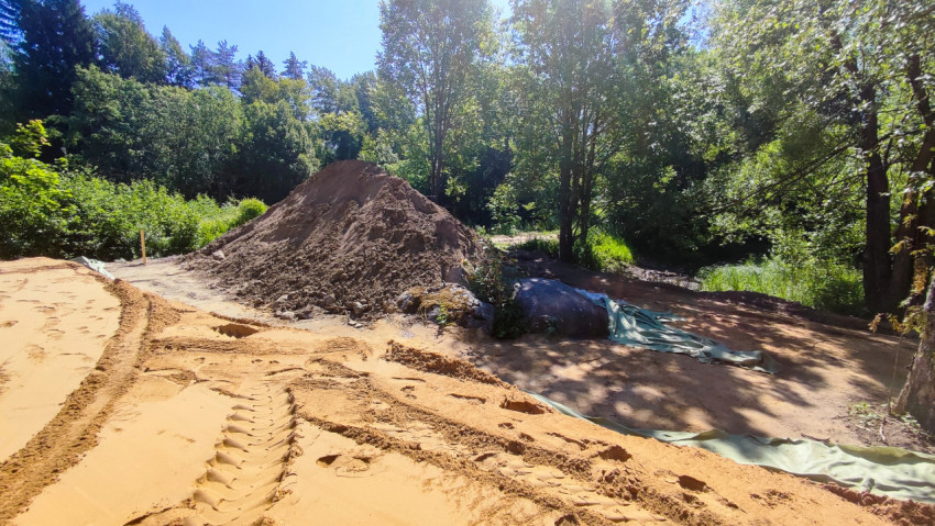 Следы техники на песке и высокий отвал грунта на лесной строительной площадке с геотекстилем