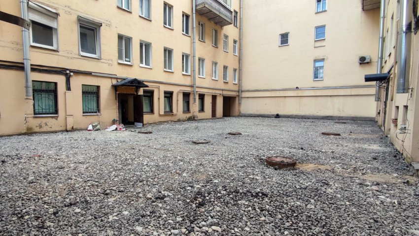 Щебёночный двор с входом под козырьком и окнами в решётках на первом этаже
