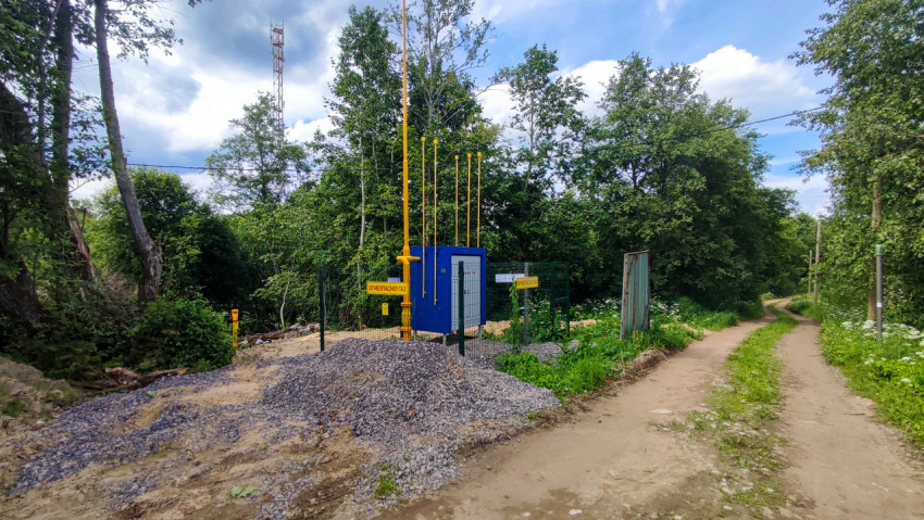 Газовый узел за ограждением у грунтовой дороги в зеленой зоне