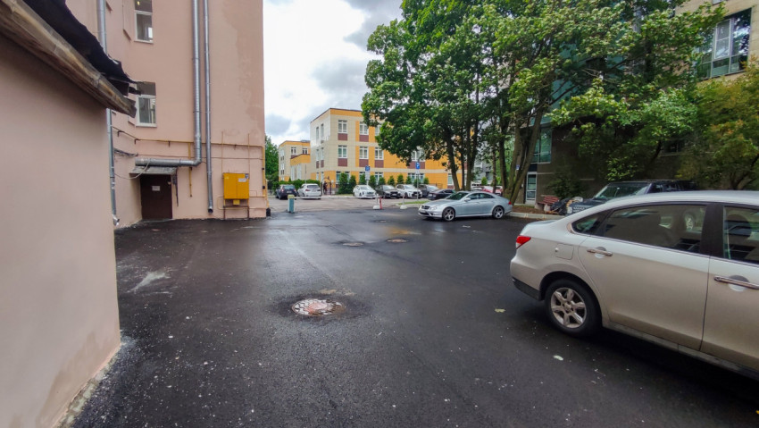 Дворовая парковка с люком на асфальте, деревьями и жилыми домами на заднем плане