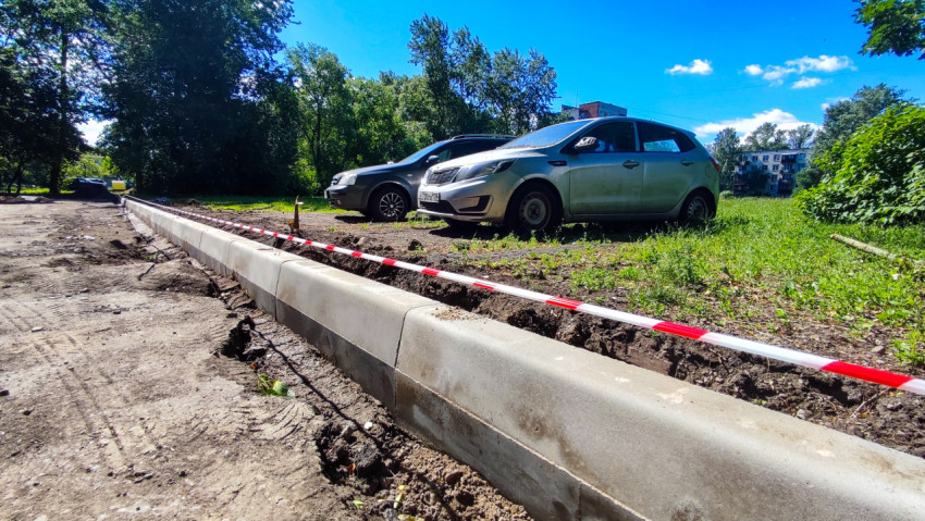 Длинная линия нового бордюра с сигнальной лентой на границе грунтовой площадки и газона