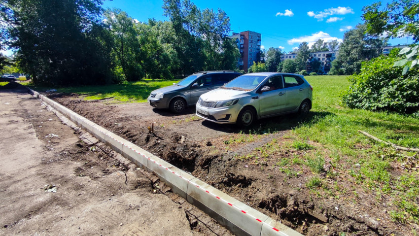 Парковочная площадка у зелёного поля и жилых домов с новым бордюром после земляных работ