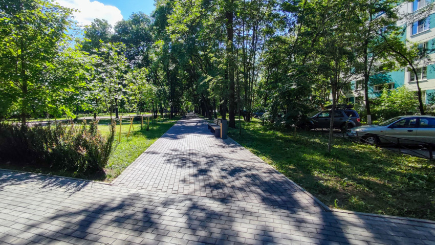 Пешеходная аллея из тротуарной плитки с лавочками и деревьями рядом с жилым домом