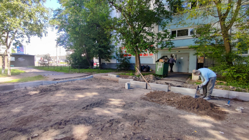 Рабочий формирует основание у бордюра возле подъезда жилого дома