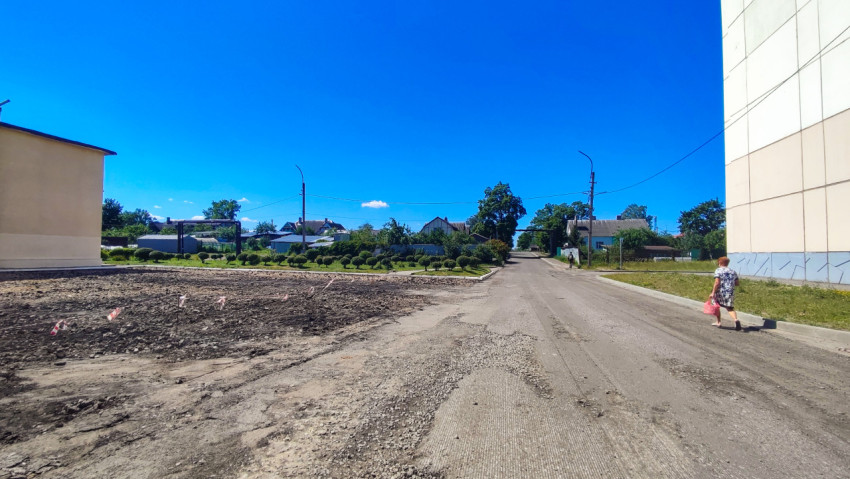 Дорога со снятым слоем асфальта у промышленных зданий с пешеходом на обочине