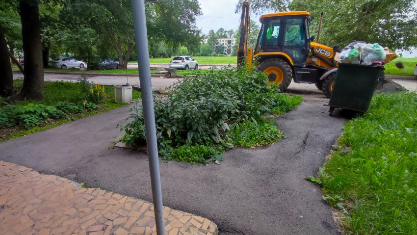 Асфальтовая дворовая дорожка с мусорным контейнером и экскаватором-погрузчиком JCB среди зелени