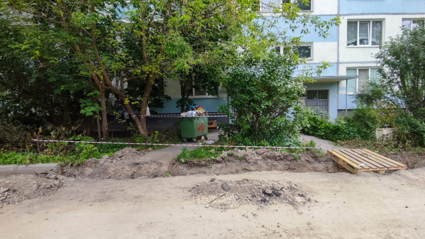 Ограждённая лентой траншея вдоль дома и поддоны на участке дворового ремонта