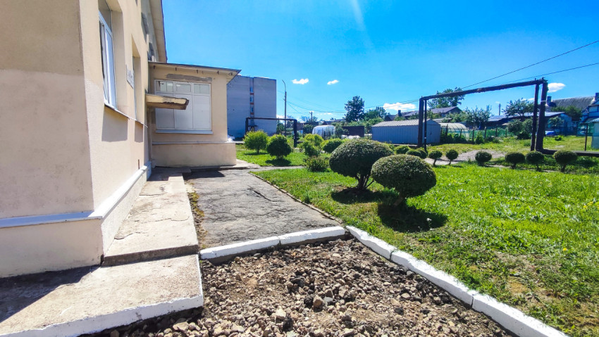 Разрушенный тротуар у здания и ухоженные кусты на газоне