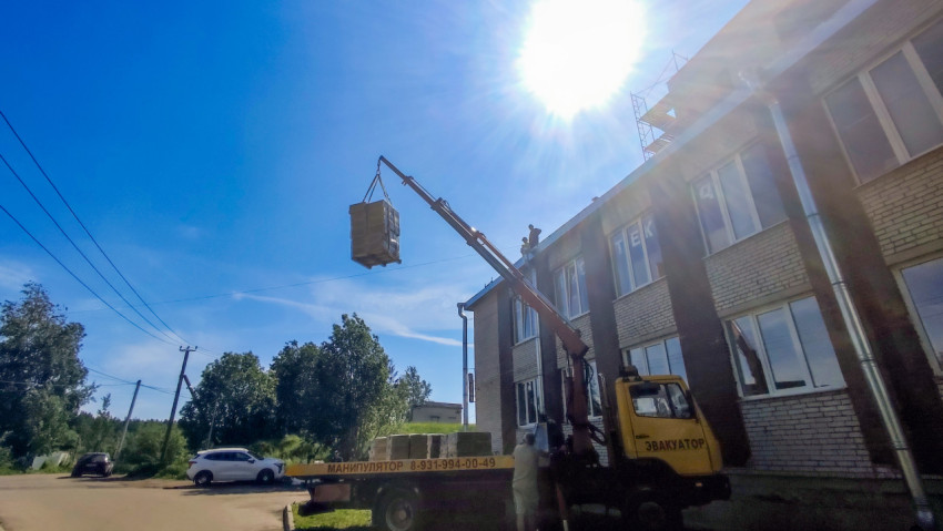 Кран-манипулятор поднимает груз у фасада здания при ярком солнце