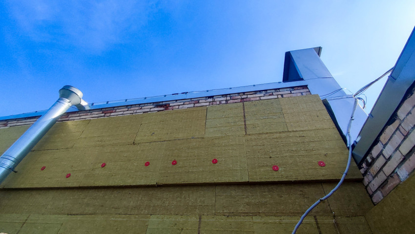 Стена с минеральной ватой, вентиляционной трубой и кабелем под кровельным отливом