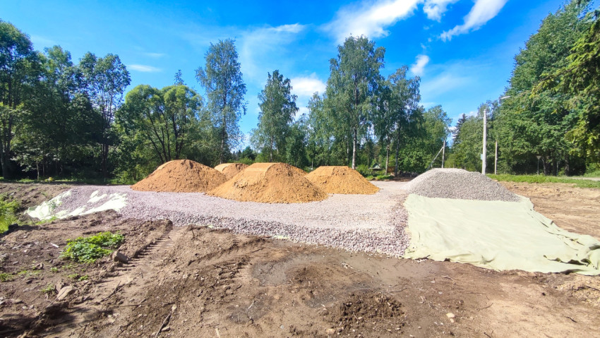 Кучи песка и щебня на геотекстиле на строительной площадке среди деревьев