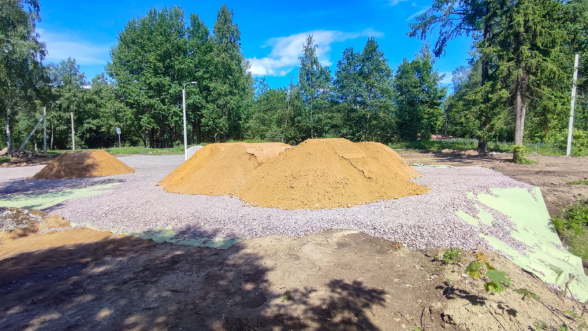 Кучи песка на щебёночной подушке с геотекстилем на фоне леса и голубого неба
