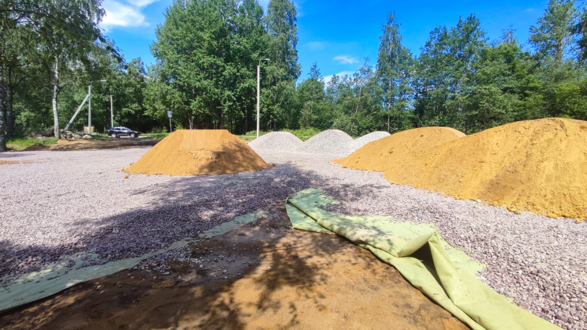 Площадка с кучами песка и щебня и свернутым геотекстилем под голубым небом